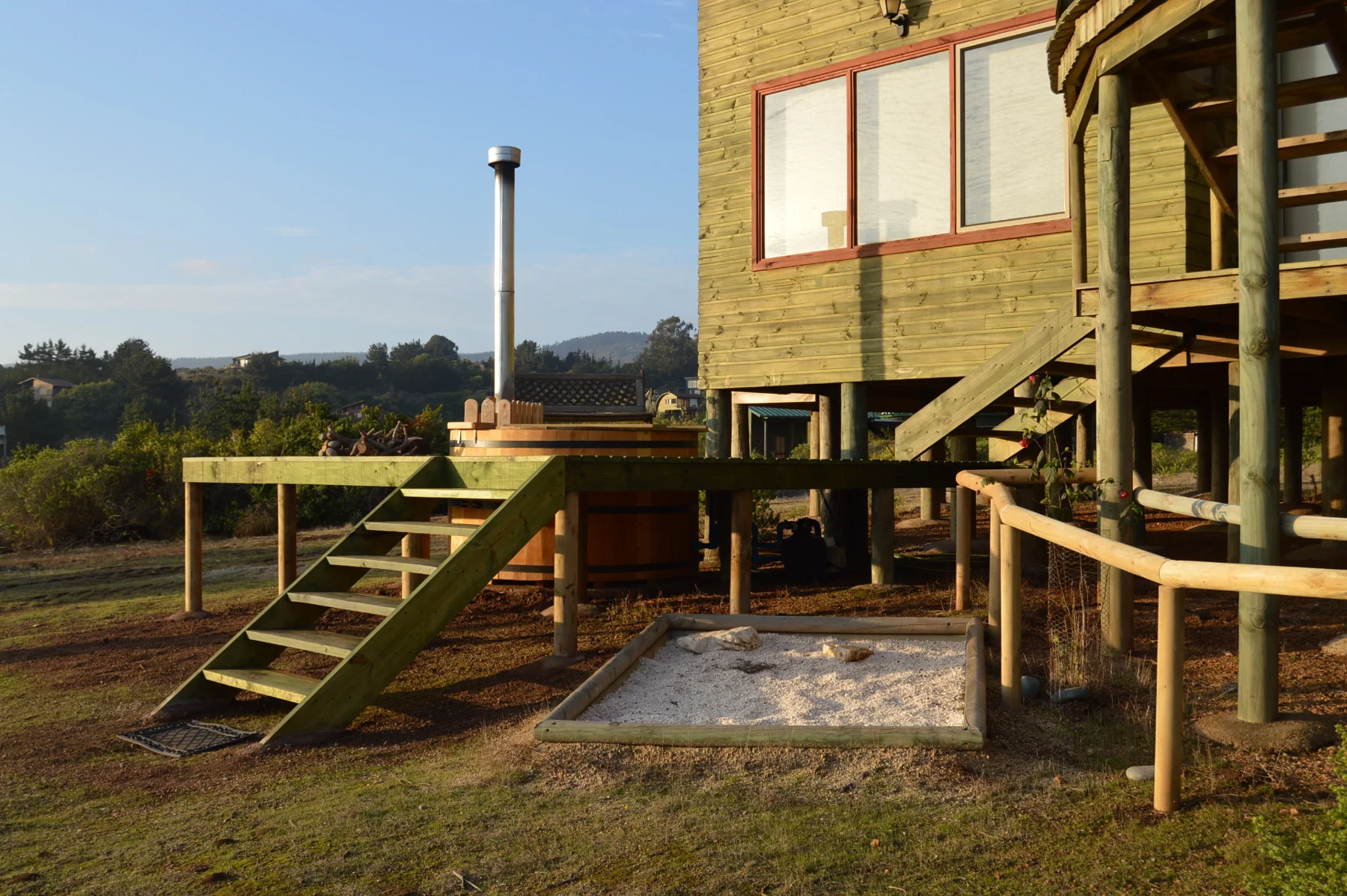 Tina sobre terraza elevada de madera con escalera junto a una vivienda