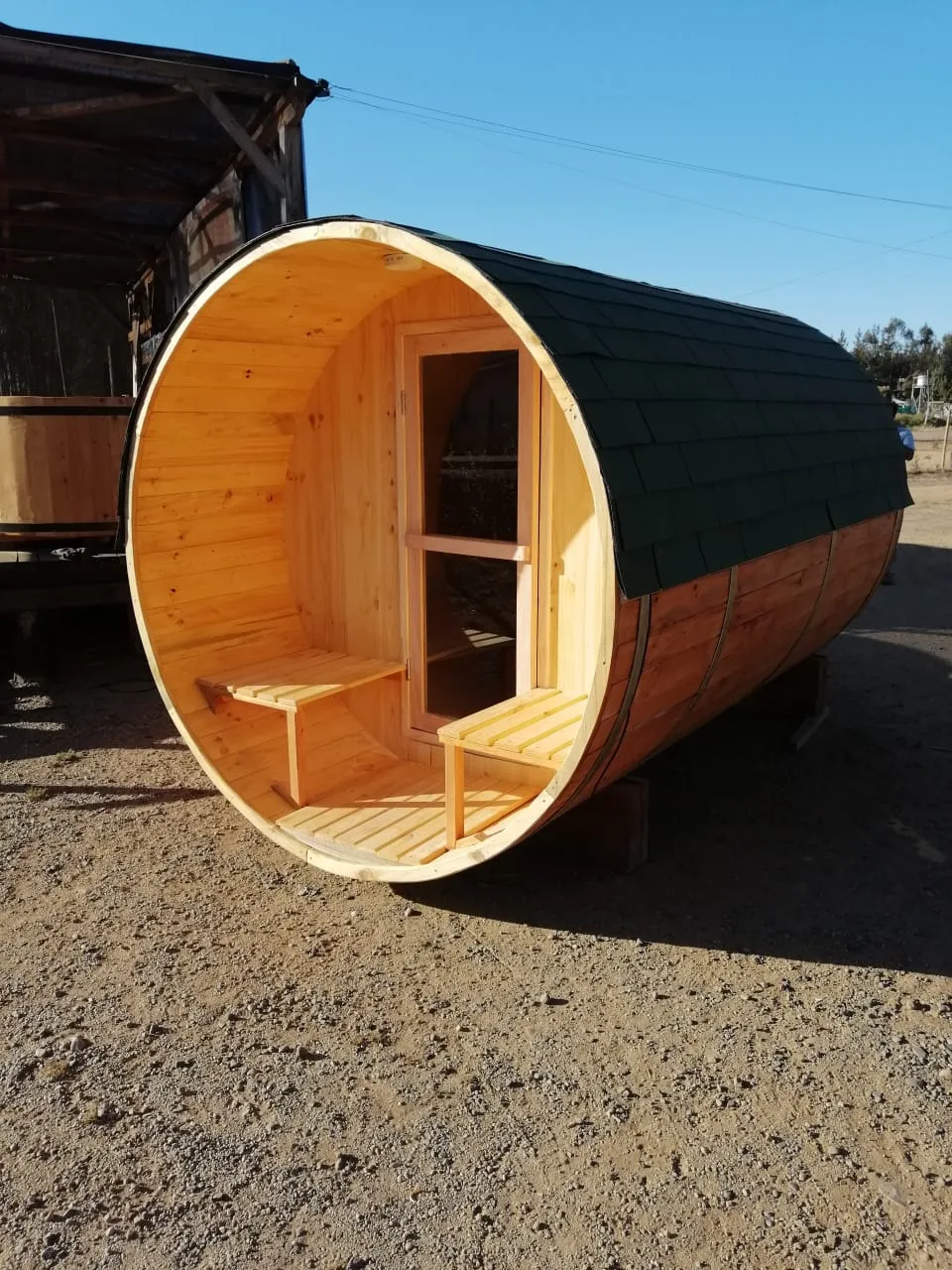 Sauna exterior de madera tipo barril con techo de tejuela verde