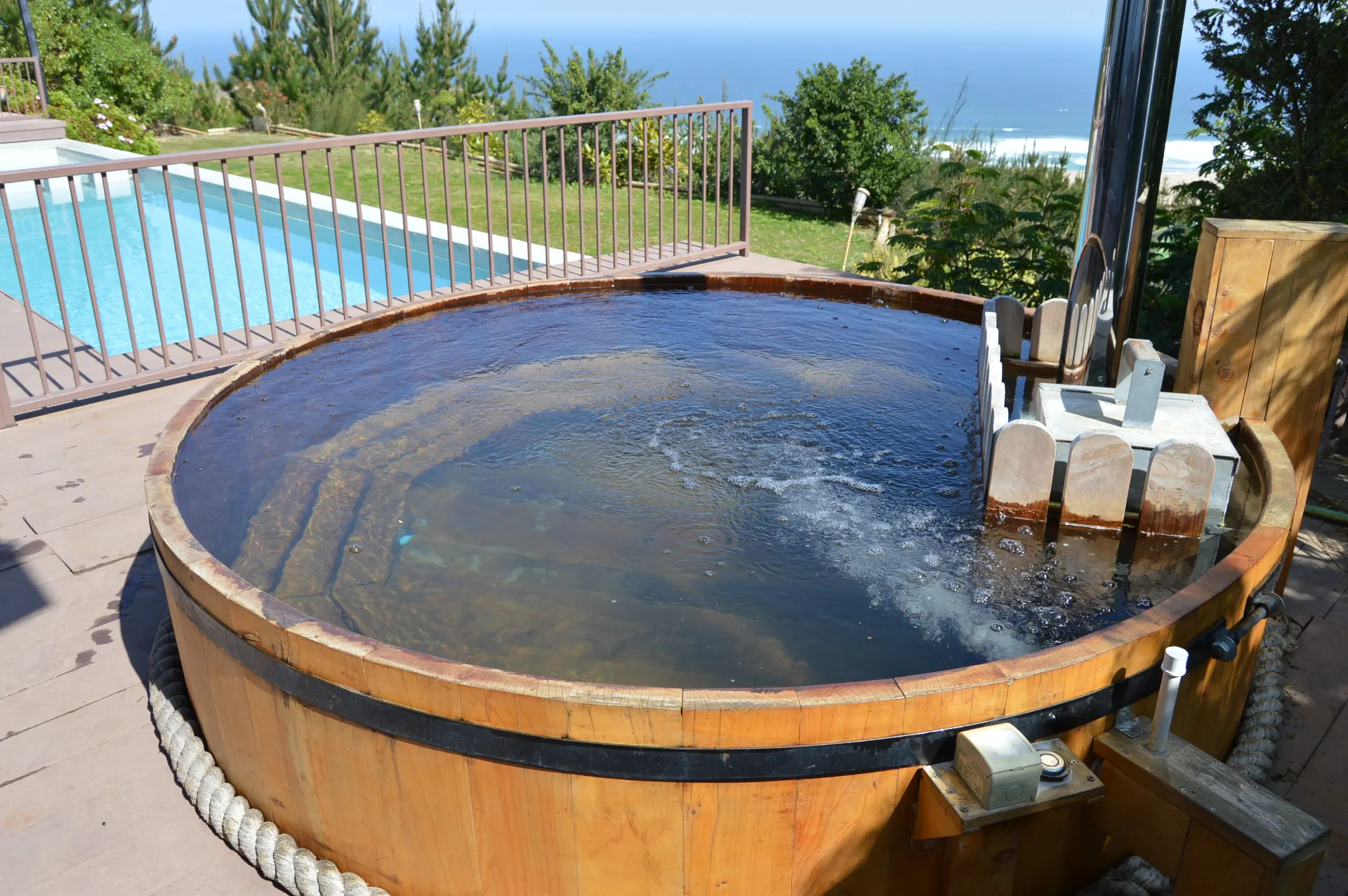 Tina de madera con hidromasaje funcionando junto a piscina y vista al mar